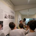 Foto de uma guia da fundação Dorina apresentando o centro de memória para um grupo de meninos