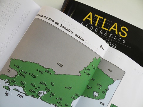 Imagem em destaque: foto de um atlas em braille. Fim da descrição.