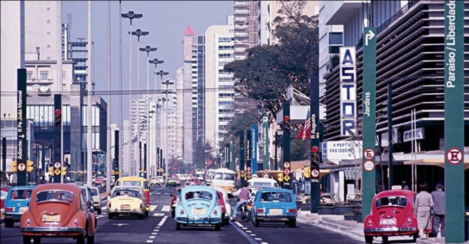 Imagem destacada: Fotografia antiga da Avenida Paulista na década de 1970. É possível ver vários carros de cores vibrantes entre Fuscas, Brasílias e Variantes. Há placas de sinalização dos bairros Jardins, Paraíso/Liberdade e uma grande placa à direita com o texto "ASTOR", na vertical. Fim da descrição. (Reprodução/Facebook São Paulo Antiga)