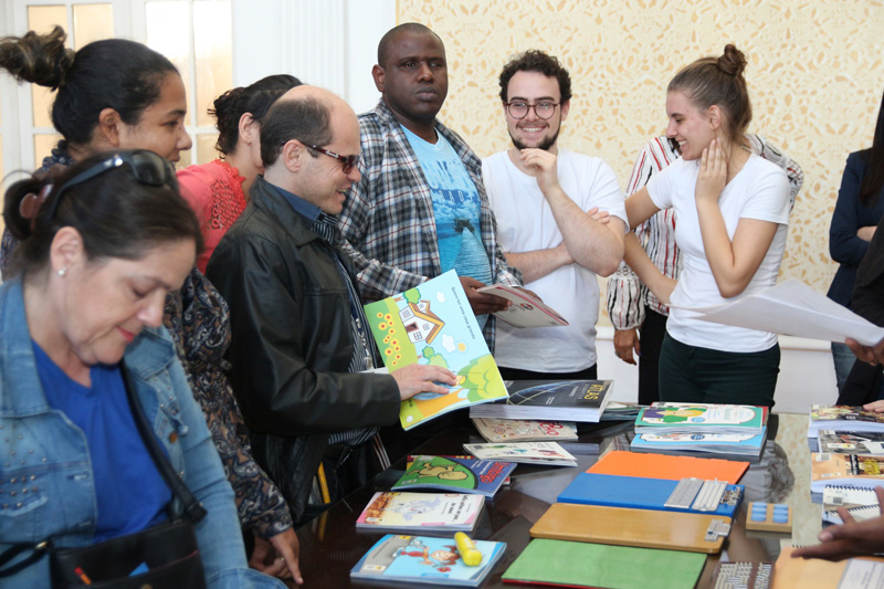 Descrição da imagem: Foto de um grupo de pessoas ao redor de uma mesa de livros.