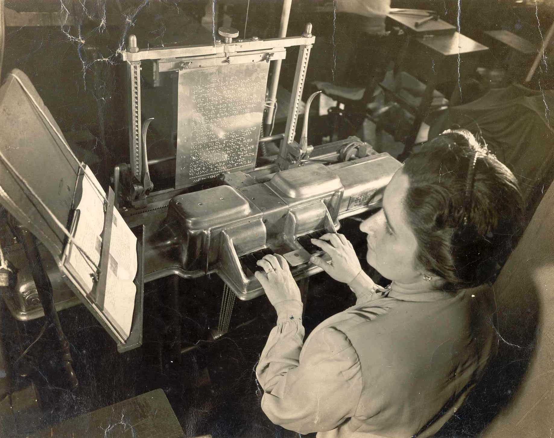 Foto em preto e branco de uma mulher fazendo a gravação de uma matriz braile para a produção de livros.