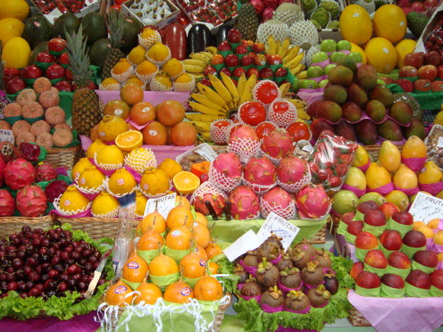 Descrição da imagem: foto de diversas frutas empilhadas em prateleiras de uma banca. Fim da descrição.