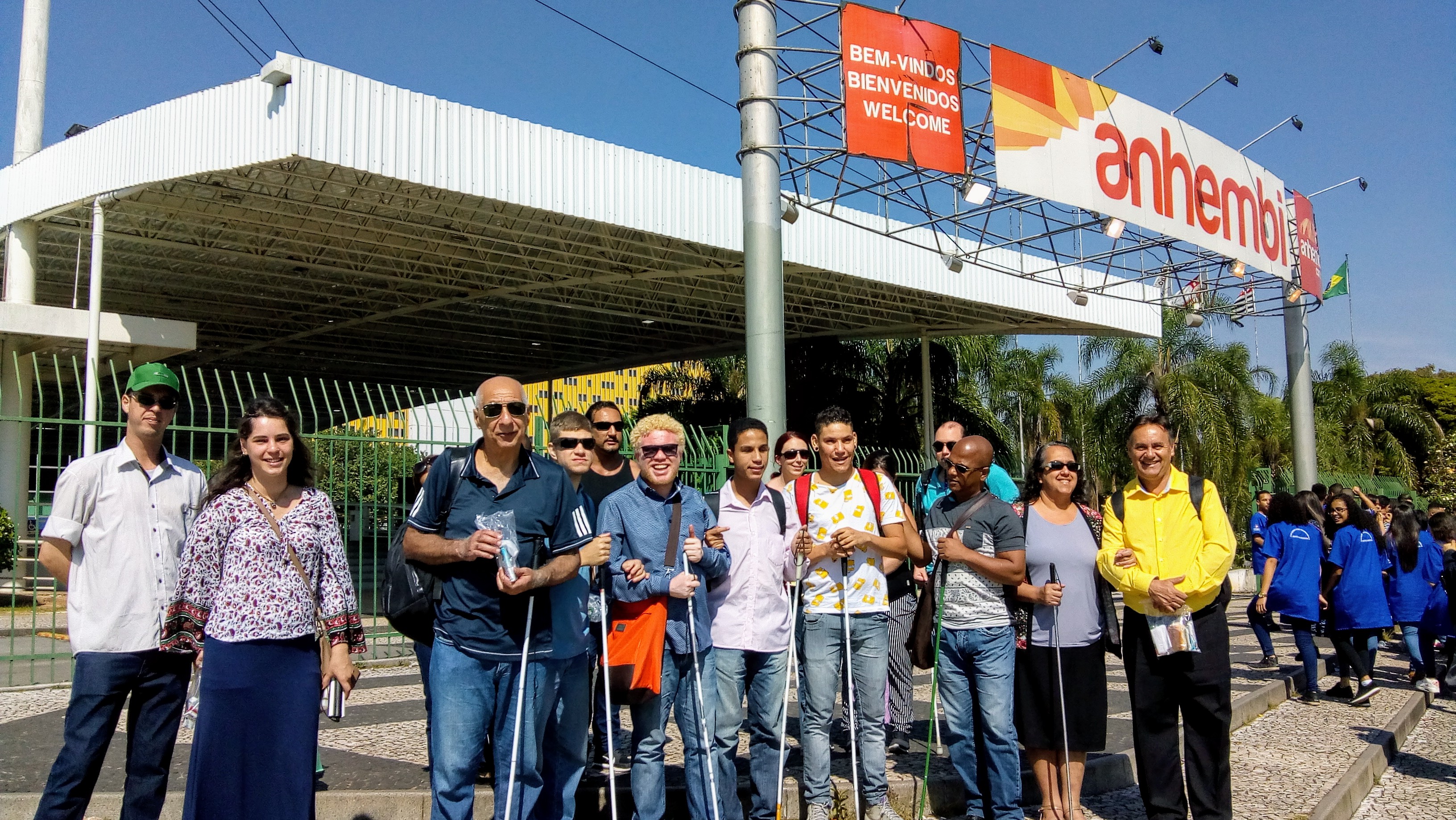 Foto de todos os alunos, ex-alunos e clientes em frente à entrada da Feira do Empreendedor. Eles olham pra frente e sorriem. Alguns seguram bengalas.