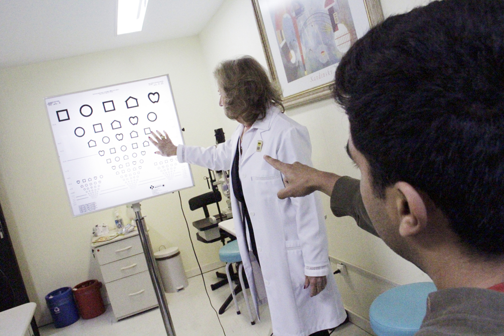 Descrição da imagem: Foto de um homem e uma médica. Ele está fazendo uma avaliação oftalmológica.