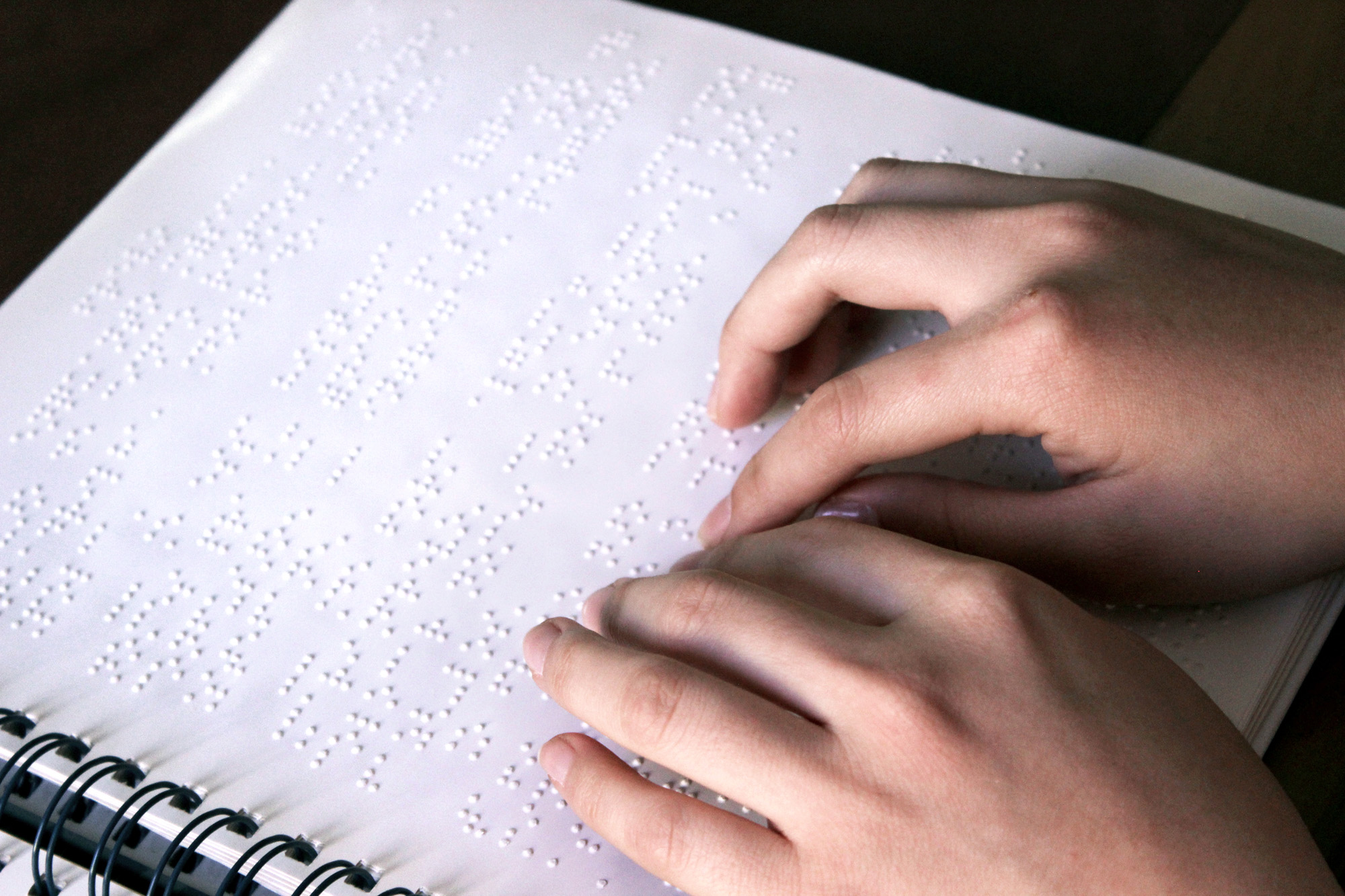 Descrição da imagem: foto de duas mãos sobre papel com texto em braille