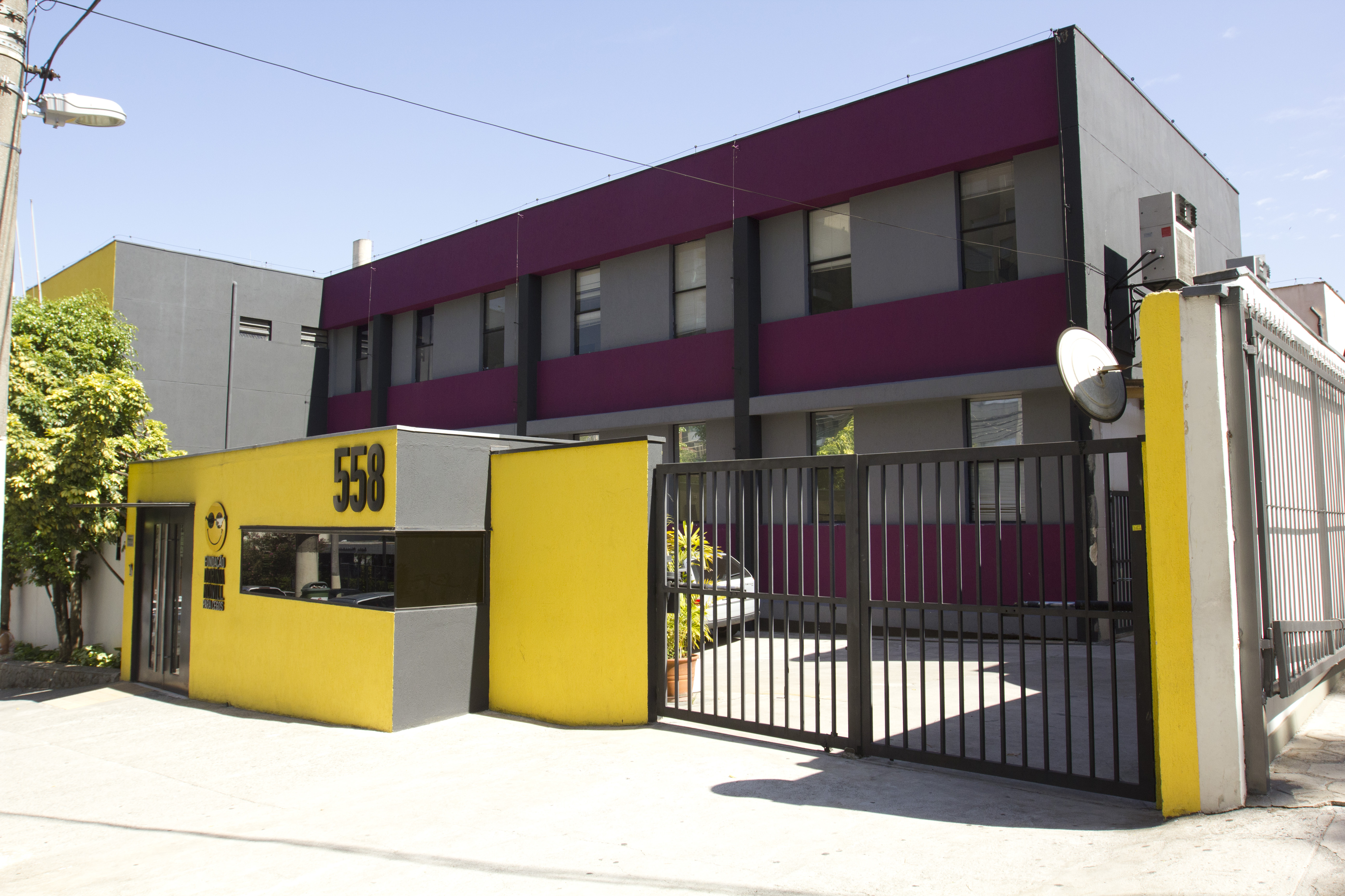 Foto da atual fachada da Fundação Dorina, com destaque para as cores amarela, cinza roxa, com o logotipo da Fundação e o número do prédio em relevos, fixados na parede. de entrada.