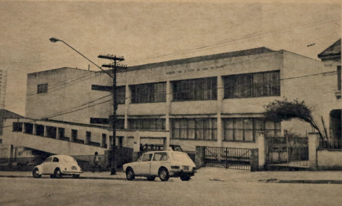 Foto antiga da fachada da então Fundação para o Livro do Cego no Brasil, na década de 1950. Em frente à Fundação estão dois carros estacionados.