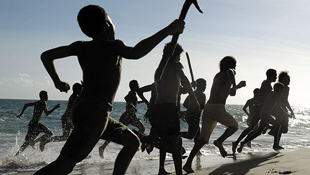 Cena do filme Capitães da Areia. Diversas crianças e adolescentes estão correndo à beira da praia, com alguns objetos nas mãos como pedaços de ferro.