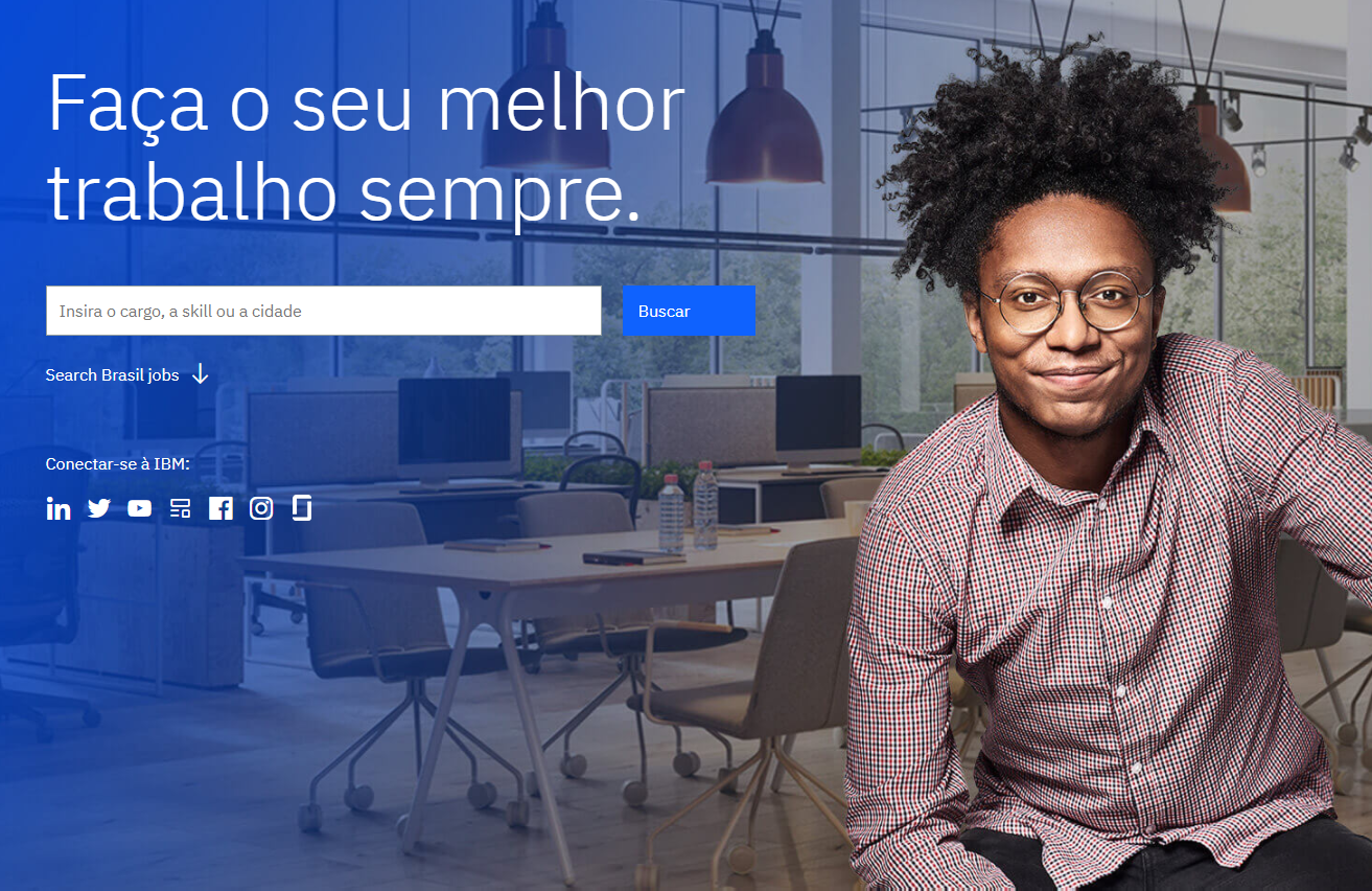 Descrição da imagem: foto de rapaz negro sorridente sentado na cadeira de um escritório. Ele usa camisa social e óculos de armação redonda. Ao lado direito há o texto "Faça o seu melhor trabalho sempre". Logo abaixo há um campo de formulário com o texto "Insira o cargo, a skill ou a cidade - Buscar", seguido por ícones de redes sociais.